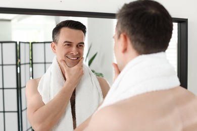 Photo of Smiling man after shaving looking at mirror in bathroom