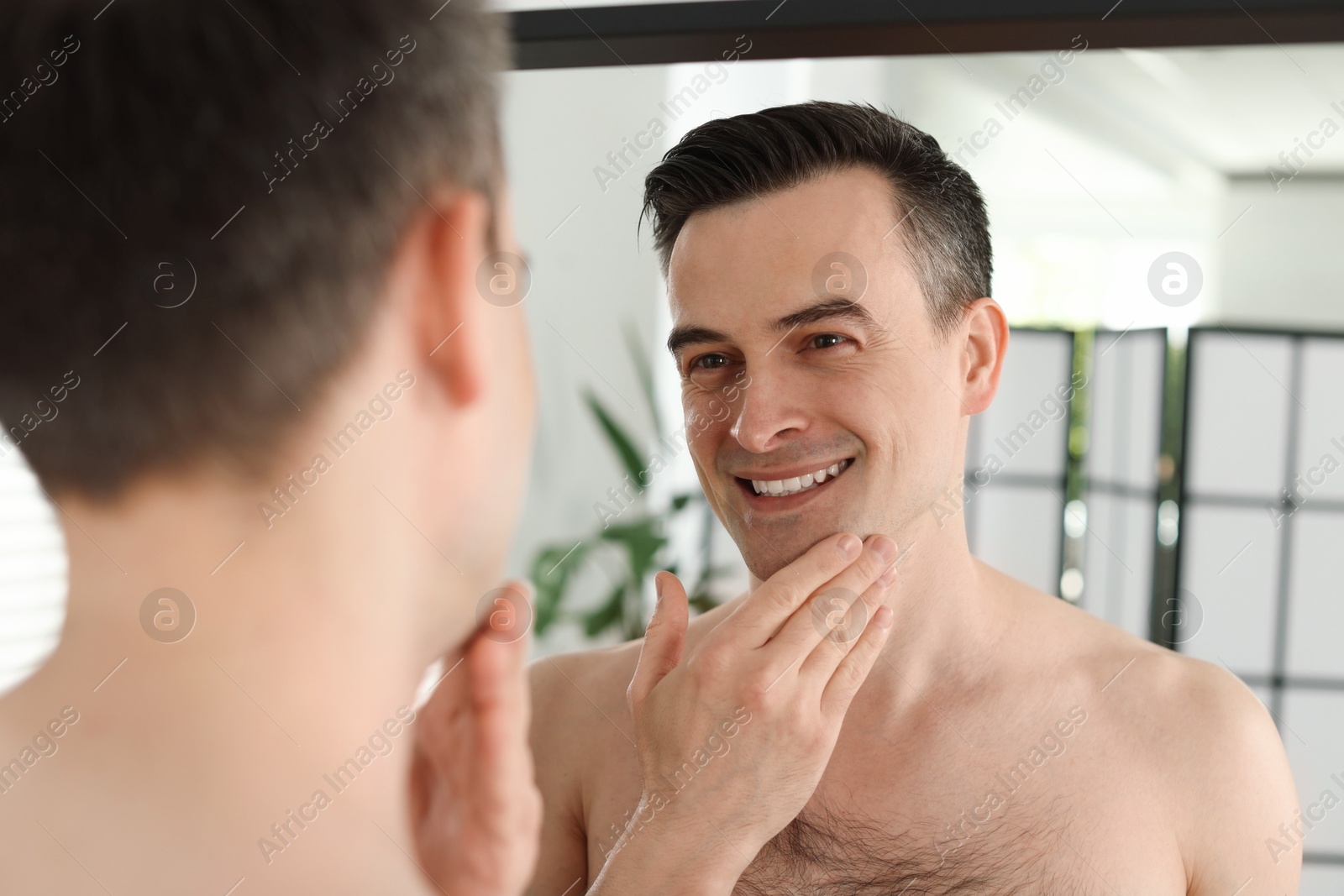 Smiling man after shaving looking at mirror in bathroom Photo of Smiling man after shaving looking at mirror in bathroom