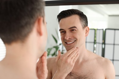 Photo of Smiling man after shaving looking at mirror in bathroom