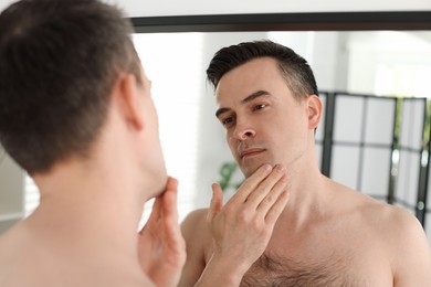 Photo of Handsome man after shaving looking at mirror in bathroom