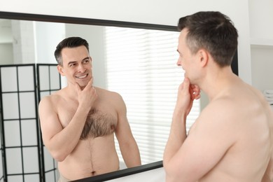 Photo of Smiling man after shaving looking at mirror in bathroom