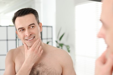 Photo of Smiling man after shaving looking at mirror in bathroom