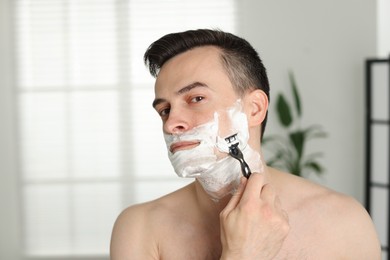 Photo of Handsome man shaving with razor at home