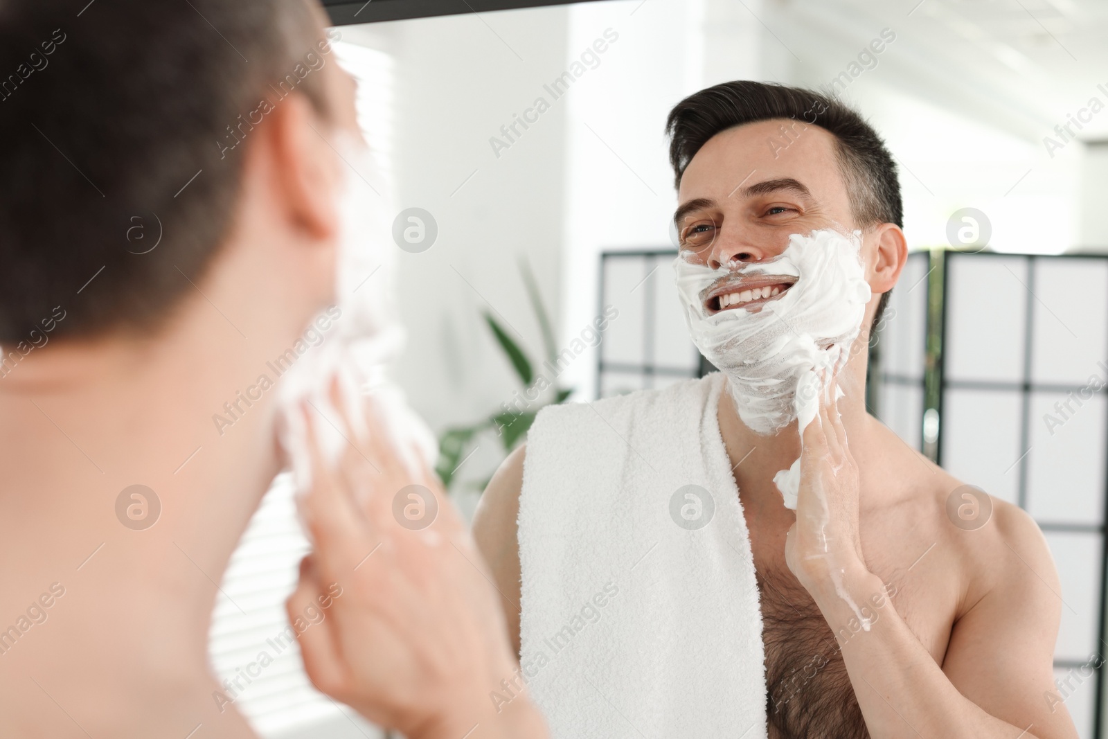 Smiling man applying shaving foam near mirror in bathroom Photo of Smiling man applying shaving foam near mirror in bathroom