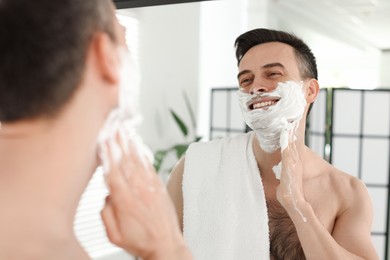 Photo of Smiling man applying shaving foam near mirror in bathroom