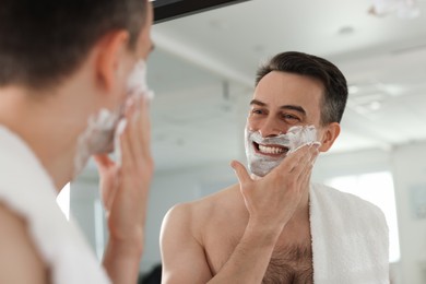 Photo of Smiling man applying shaving foam near mirror at home, low angle view