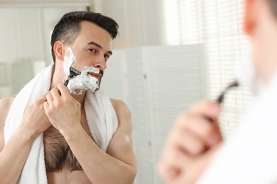 Photo of Handsome man shaving with razor near mirror at home