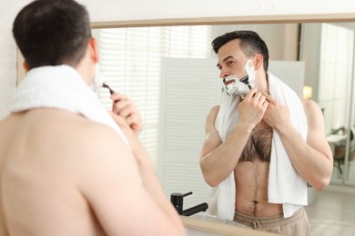 Photo of Handsome man shaving with razor near mirror at home