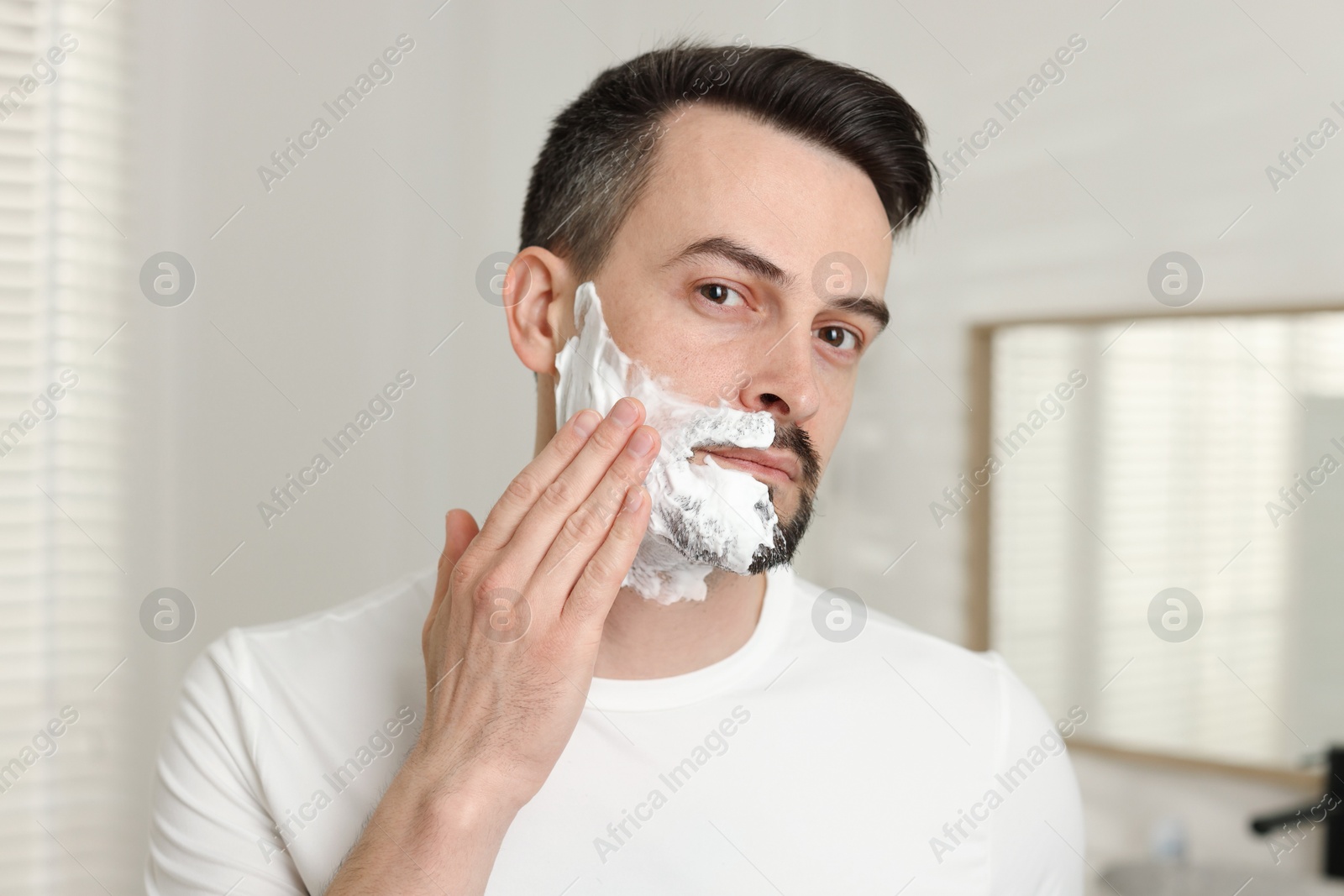 Handsome man applying shaving foam in bathroom Photo of Handsome man applying shaving foam in bathroom