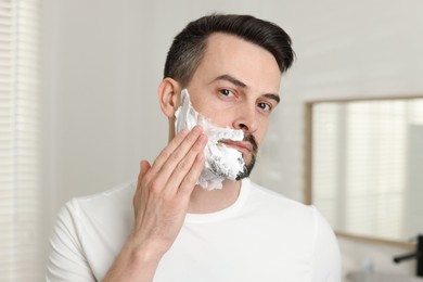 Photo of Handsome man applying shaving foam in bathroom