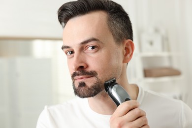Photo of Handsome man shaving with trimmer at home, closeup