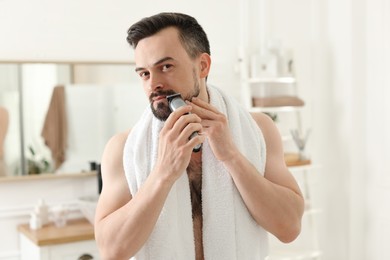 Photo of Handsome man shaving with trimmer in bathroom