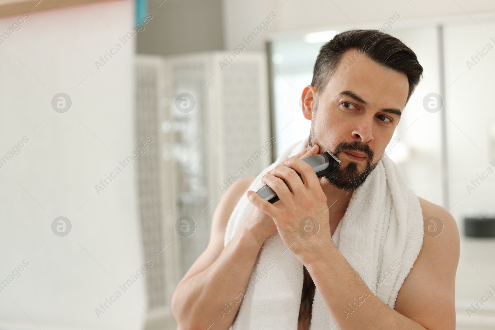 Handsome man shaving with trimmer near mirror at home. Space for text Photo of Handsome man shaving with trimmer near mirror at home. Space for text