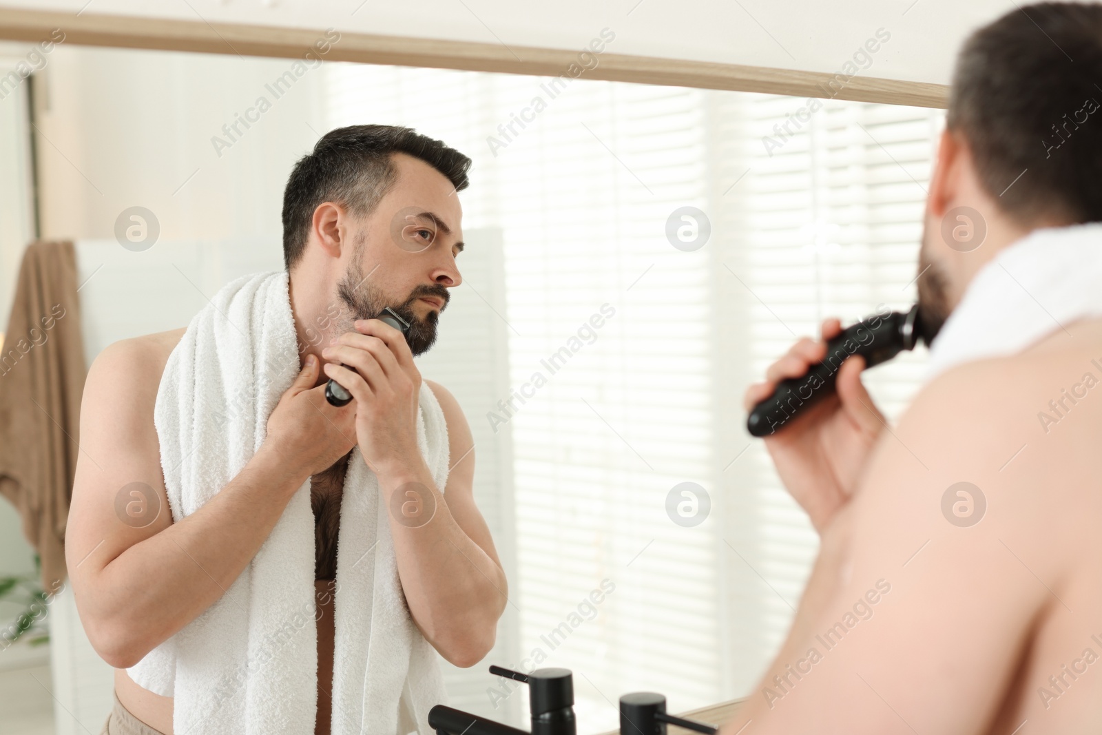 Handsome man shaving with trimmer near mirror in bathroom Photo of Handsome man shaving with trimmer near mirror in bathroom