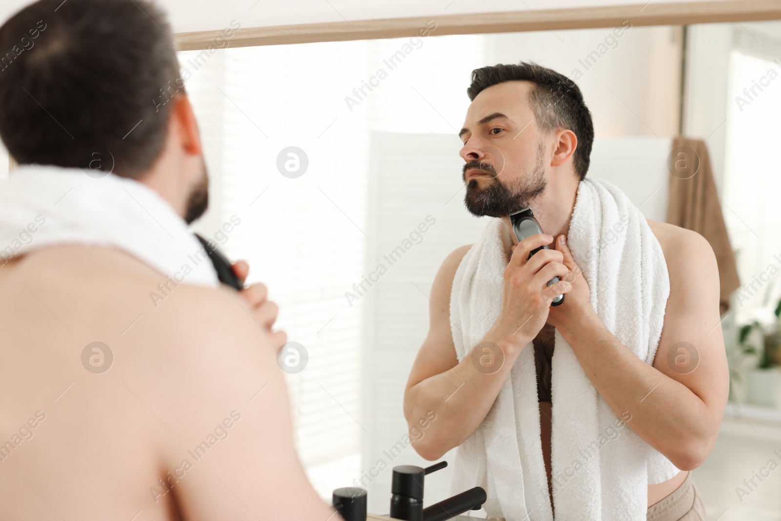Handsome man shaving with trimmer near mirror in bathroom Photo of Handsome man shaving with trimmer near mirror in bathroom