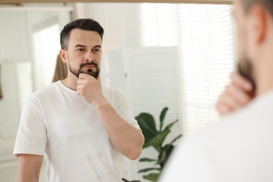 Photo of Handsome man before shaving looking at mirror in bathroom