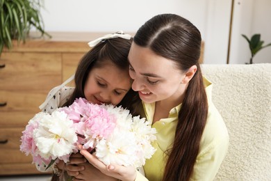 Photo of Cute little girl giving her mother bouquet of beautiful peonies at home