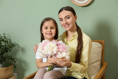 Photo of Mother and her daughter with bouquet of beautiful peonies at home