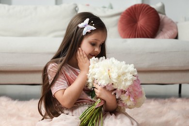 Photo of Cute little girl with bouquet of beautiful peonies on floor at home