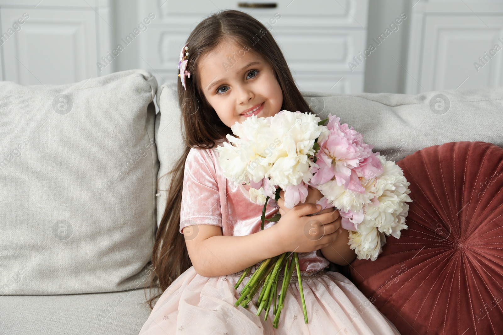 Cute little girl with bouquet of beautiful peonies on sofa at home Photo of Cute little girl with bouquet of beautiful peonies on sofa at home