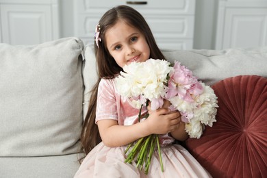 Photo of Cute little girl with bouquet of beautiful peonies on sofa at home