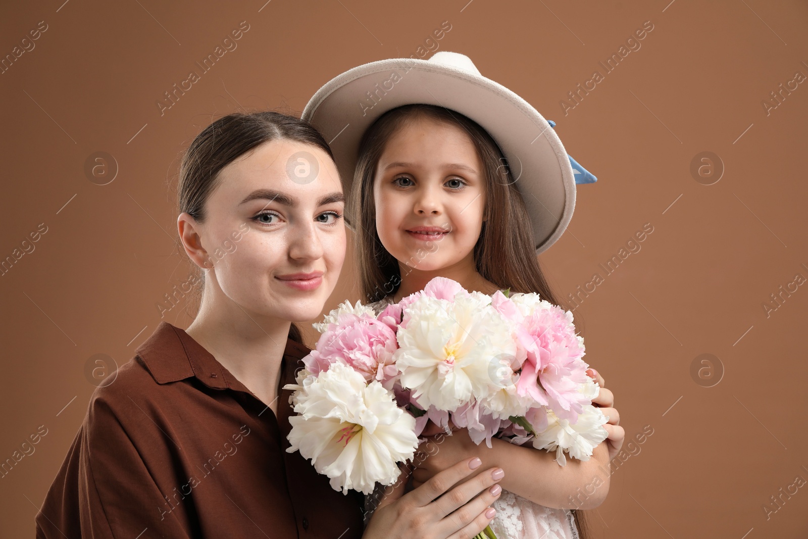 Mother and her daughter with bouquet of beautiful peonies on brown background Photo of Mother and her daughter with bouquet of beautiful peonies on brown background