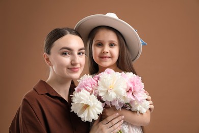 Photo of Mother and her daughter with bouquet of beautiful peonies on brown background