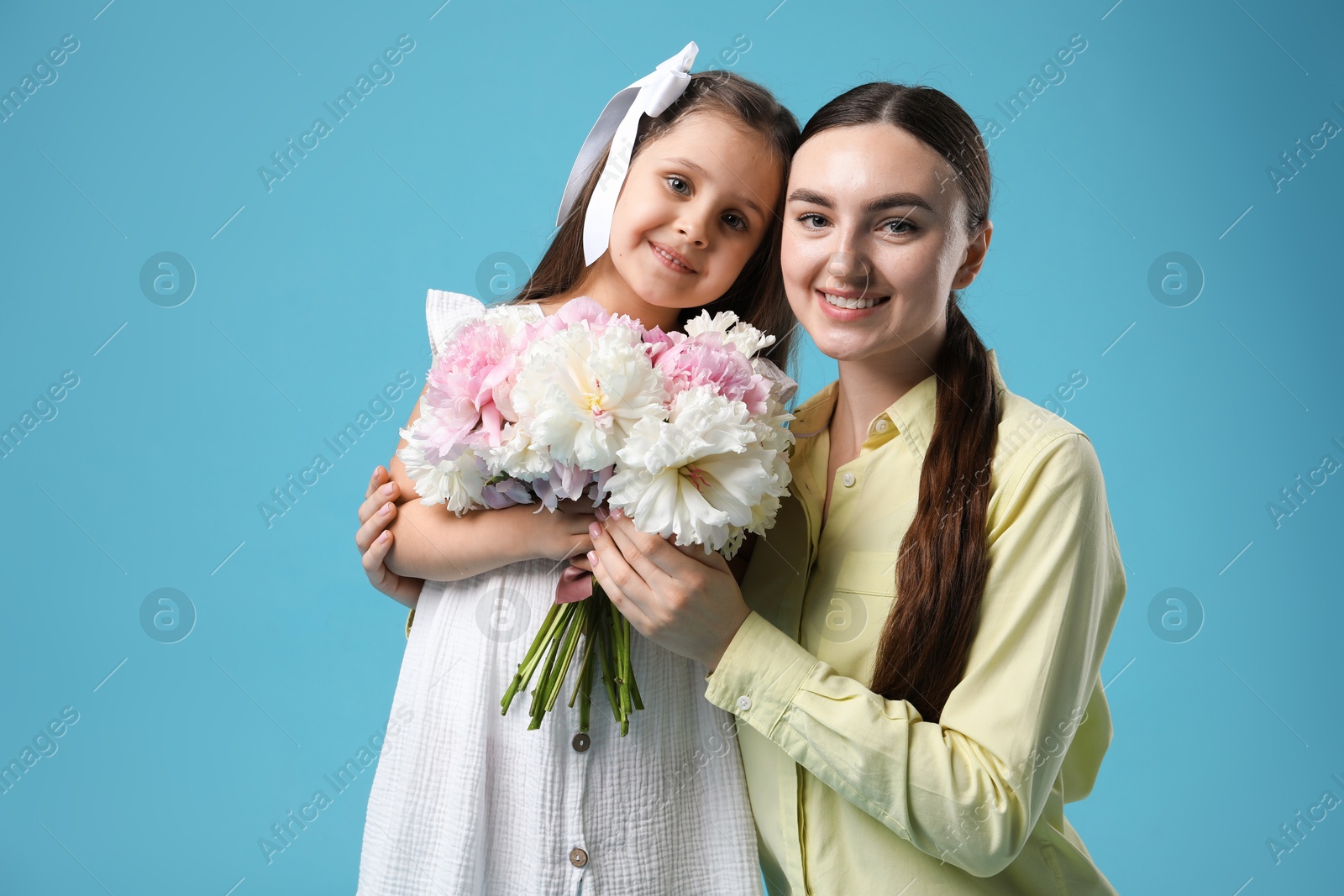 Mother and her daughter with bouquet of beautiful peonies on light blue background Photo of Mother and her daughter with bouquet of beautiful peonies on light blue background