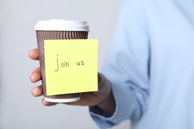 Photo of Join Us. Woman holding takeaway cup with sticky note on grey background, closeup