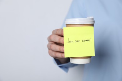 Photo of Join Our Team. Woman holding takeaway cup with sticky note on grey background, closeup. Space for text