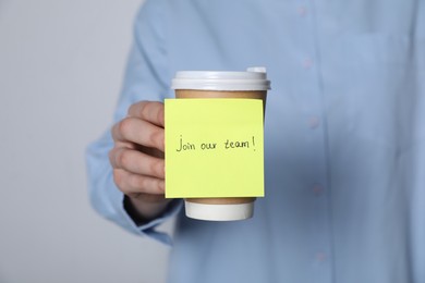 Photo of Join Our Team. Woman holding takeaway cup with sticky note on grey background, closeup