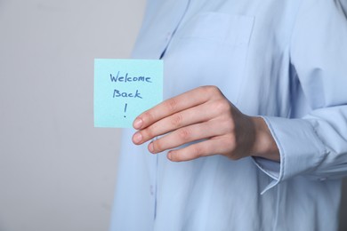 Photo of Woman holding paper note with words Welcome Back on grey background, closeup