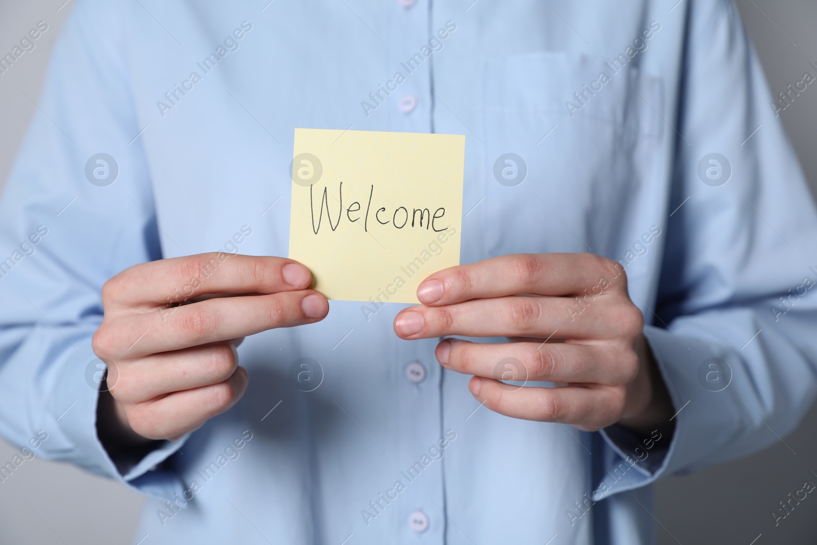 Woman holding paper note with word Welcome on grey background, closeup Photo of Woman holding paper note with word Welcome on grey background, closeup
