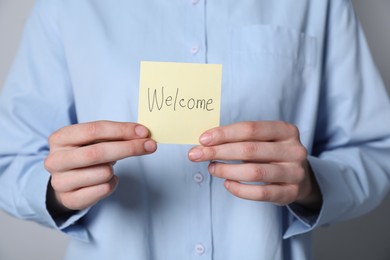 Photo of Woman holding paper note with word Welcome on grey background, closeup