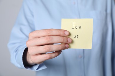 Photo of Woman holding paper note with words Join Us on grey background, closeup