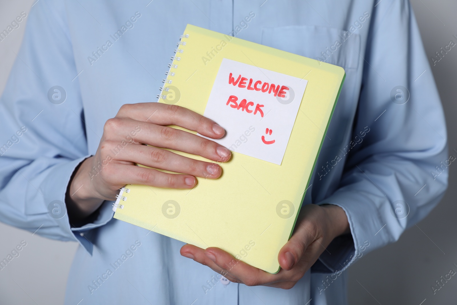 Photo of Welcome Back. Woman holding notepad with sticky note on grey background, closeup