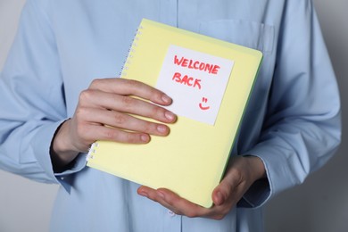 Photo of Welcome Back. Woman holding notepad with sticky note on grey background, closeup