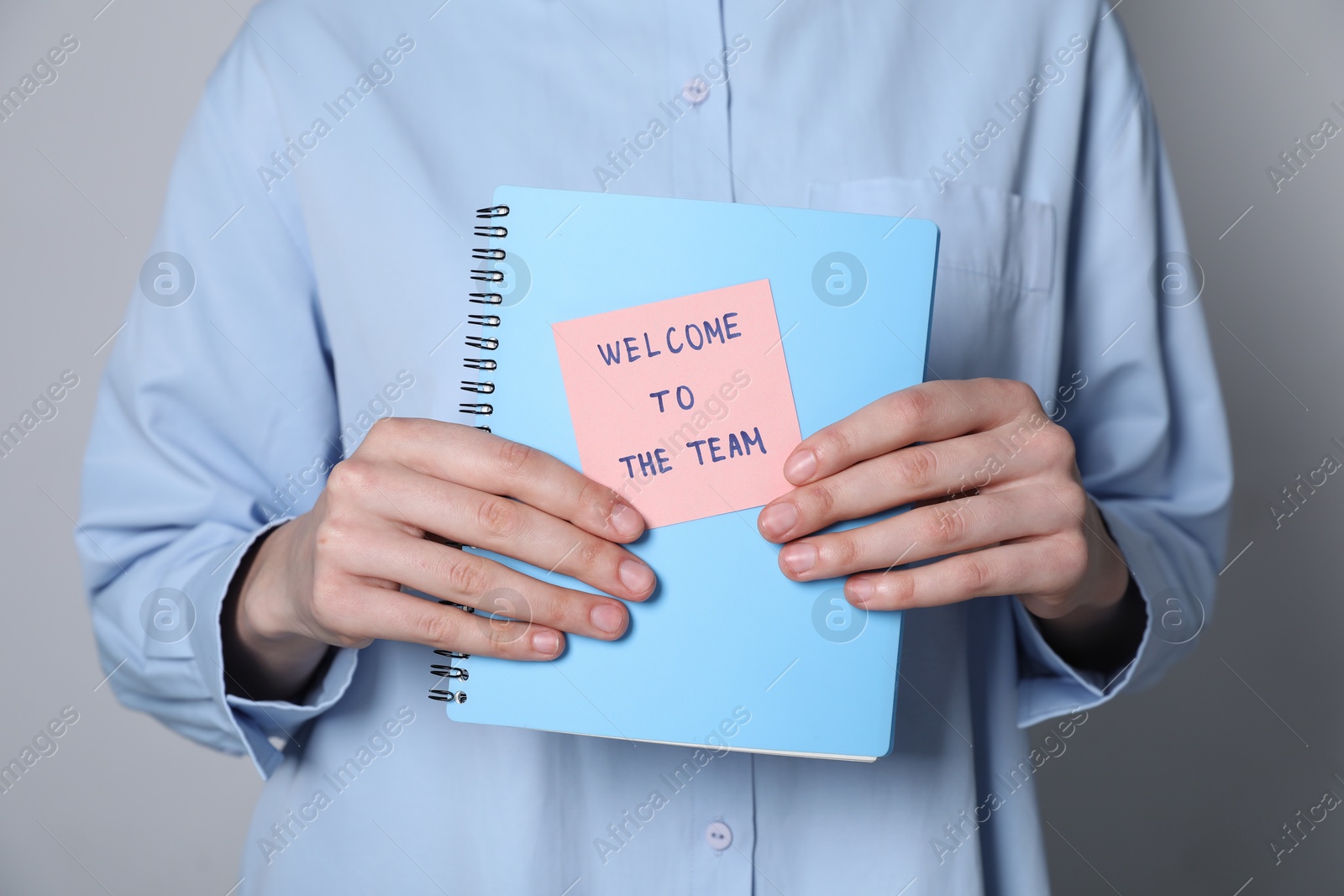 Welcome To The Team. Woman holding notepad with sticky note on grey background, closeup Photo of Welcome To The Team. Woman holding notepad with sticky note on grey background, closeup