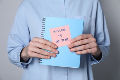 Photo of Welcome To The Team. Woman holding notepad with sticky note on grey background, closeup