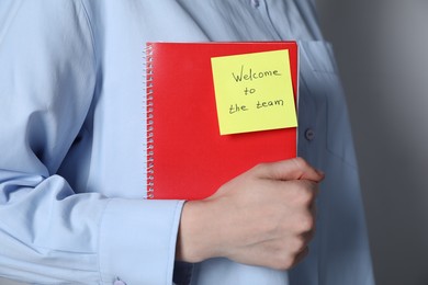 Photo of Welcome To The Team. Woman holding notepad with sticky note on grey background, closeup