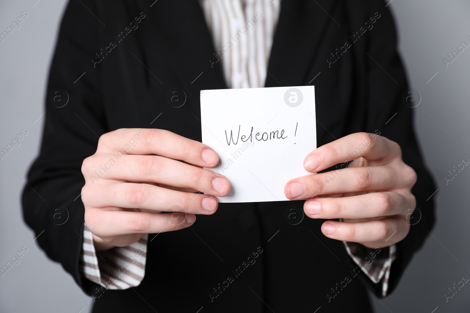 Photo of Human resources manager holding sticky note with word Welcome on grey background, closeup