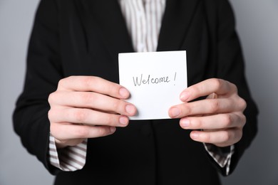 Photo of Human resources manager holding sticky note with word Welcome on grey background, closeup