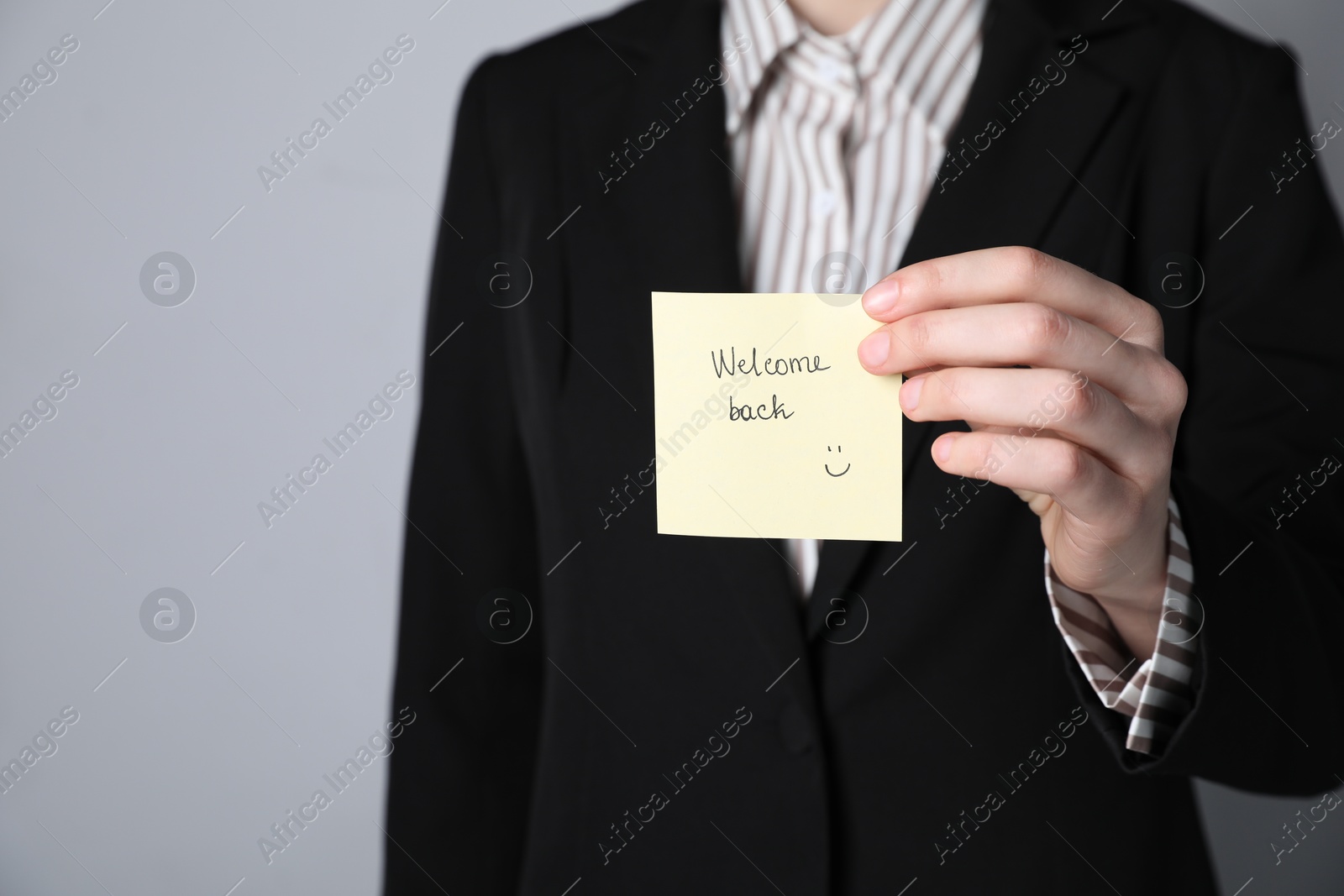 Businesswoman holding sticky note with word Welcome Back on grey background, closeup. Space for text Photo of Businesswoman holding sticky note with word Welcome Back on grey background, closeup. Space for text
