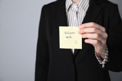 Photo of Businesswoman holding sticky note with word Welcome Back on grey background, closeup. Space for text