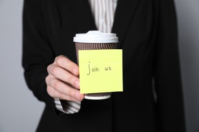 Photo of Join Us. Human resources manager holding takeaway cup with sticky note on grey background, closeup