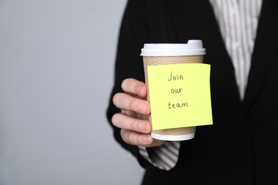 Photo of Join Our Team. Human resources manager holding takeaway cup with sticky note on grey background, closeup. Space for text