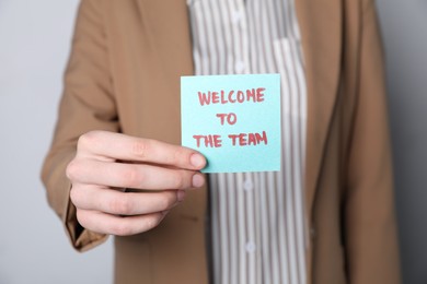 Photo of Human resources manager holding sticky note with word Welcome To The Team on grey background, closeup