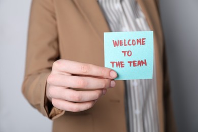 Photo of Human resources manager holding sticky note with word Welcome To The Team on grey background, closeup