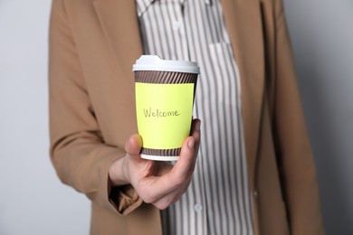 Photo of Welcome. Human resources manager holding takeaway cup with sticky note on grey background, closeup