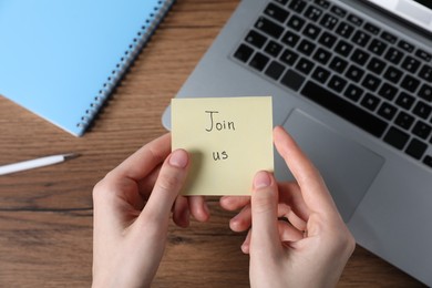 Photo of Woman holding paper note with word Join Us at wooden table, top view